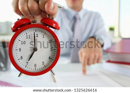 Male hand on the alarm clock a red color stands in the office on the table showing seven o'clock in the morning or evening AM PM