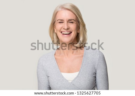 Cheerful happy mature old beautiful woman laughing at funny joke, joyful senior mid aged lady enjoying laughter with healthy dental smile having fun isolated on white grey blank studio background