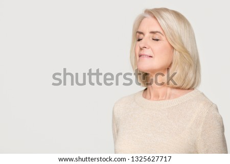Calm happy mature mid aged woman inhaling taking deep breath of fresh air feel no stress, mindful old lady meditating relaxing advertise freshener isolated on white grey studio background, copy space