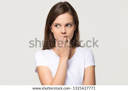 Nervous insecure young woman looking aside feeling fear uncertainty worried scared biting nails, stressed shy doubtful teen girl student anxious about problem isolated on white grey studio background Royalty-Free Stock Photo #1325627771