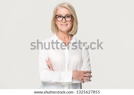 Beautiful confident mature middle aged businesswoman in glasses looking at camera posing isolated on white grey studio background, smiling older senior female professional lawyer business portrait