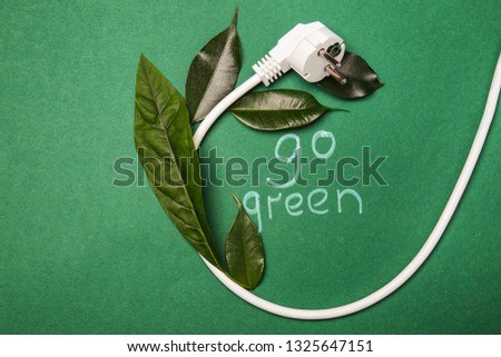 Electrical plug with leaves and text GO GREEN on color background