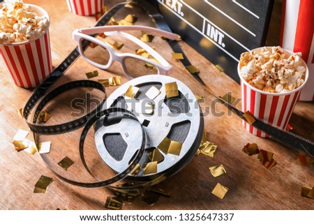 Film reel with popcorn and glasses on wooden table