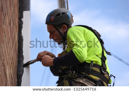 Rope access abseiler handy man building painter commercial services wearing full  safety body harness abseiling ascending hanging using brush painting down pipe  hight rise building site Sydney CBD, 