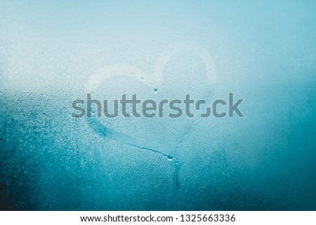 Love heart sign and foggy condensated window with blurry effect textured outdoors background, close up image