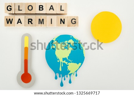 paper cut melting earth and sun, thermometer with high temperature indication on scale, and wooden cubes with "global warming" lettering on grey background