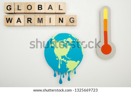 paper cut melting earth, wooden cubes with "global warming" lettering, and thermometer with hign temperature indication on scale on grey background