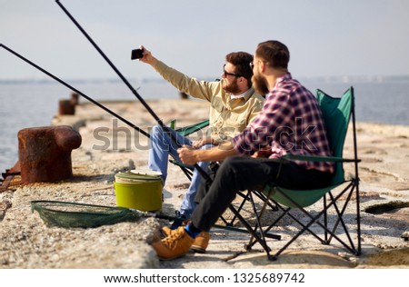 leisure and people concept - friends with fishing rods taking selfie by smartphone on pier at sea