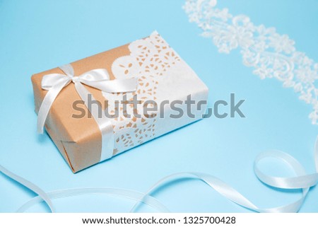 Kraft paper gift decorated with a lace napkin on a blue paper background. Holiday greeting card