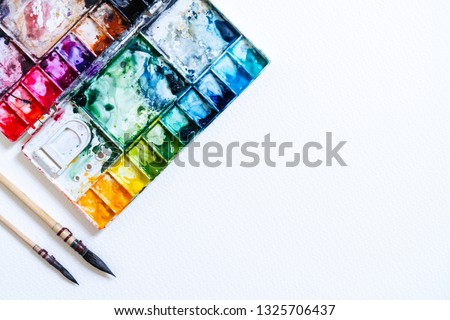 Watercolor in palette with blobs of paint and a brush. Vintage stylized photo with white texture. Copy space for add text or art work designs.