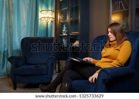 Photo of woman psychologist with tablet in hand sitting at blue chair.