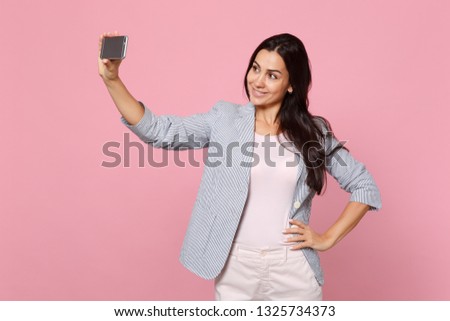 Portrait of stunning pretty young woman in striped jacket doing selfie shot on mobile phone isolated on pink pastel background in studio. People sincere emotions lifestyle concept. Mock up copy space