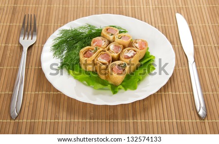Flapjack with salmon, salad, fork and knife on bamboo napkin