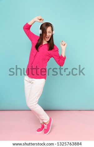 Full length portrait of young fun woman in rose shirt blouse, white pants, headphones dancing isolated on bright pink blue pastel wall background studio. Fashion lifestyle concept. Mock up copy space