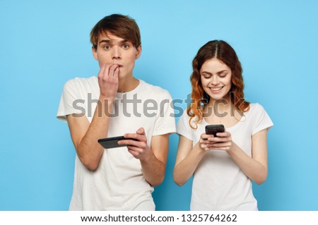 Cute guy and girl are looking into the phones and chatting with each other on a blue background