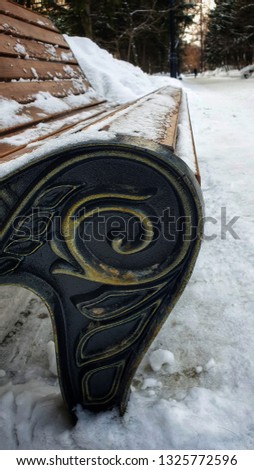 Snow-covered bench in the city square in winter. Park wooden wrought sidewalls bench with aged wrought sidewalls.