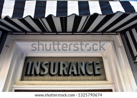 A vintage sign in silver type on a transom window reads INSURANCE, while a bold black and white awning flutters overhead.