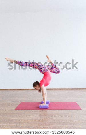 A young gymnast girl stands on her hands with her legs bent at the top.