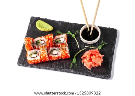 Concept of Japanese cuisine. Roll with crab sticks, cucumber and celery, with red caviar. Near soy sauce, ginger and wasabi. Modern serving dishes in the restaurant on a black slate blackboard. Ìàñàãî