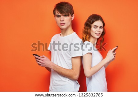 Cute man and woman with phones in their hands communicate with each other on an orange background