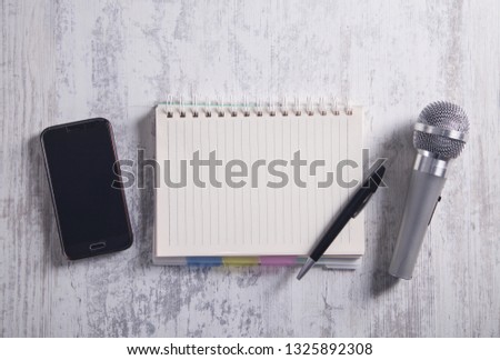 Microphone, smartphone, notepad and pen on the modern desk.