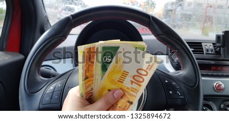Israeli money stack of new shekels banknotes of 100, 50 in female hand on sport car wheel