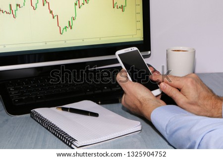 the trader in office looks at the charts and takes notes with a pen in his notebook. Next is a smartphone