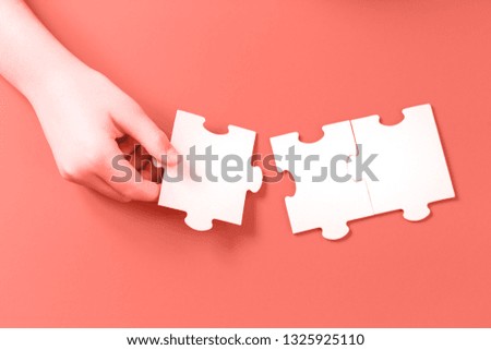 Hand with Jigsaw puzzle matching pieces. Teamwork and solution or idea concept with copy space on trendy living coral background