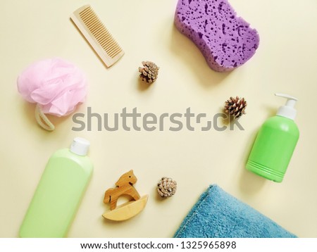 Still life photography, flat lay composition. Baby bath products for hair and skin care. Green shampoo bottle, liquid soap, purple and pink sponges, comb, wooden toy horse and towel