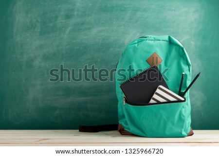 Education concept - blue backpack, black notebooks and pencils on the background of the blackboard