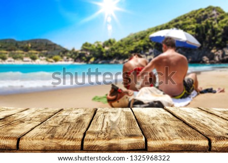 Wooden desk of free space for your decoration. Two young lovers on sand . Beach landscape with sun on blue sky. Summer time. 
