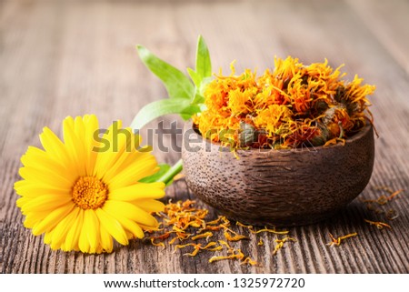 Dried and fresh marigold (calendula) flowers in a bowl on wooden rustic background space for text close-up. Herbal healthy flower tea, alternative medicine.