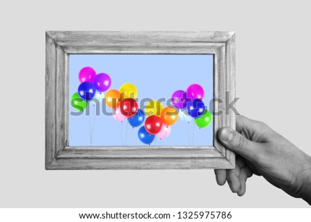 Hand holding a old picture frame with  colorful ballons color image.  Conceptual B&W image and color image in frame.