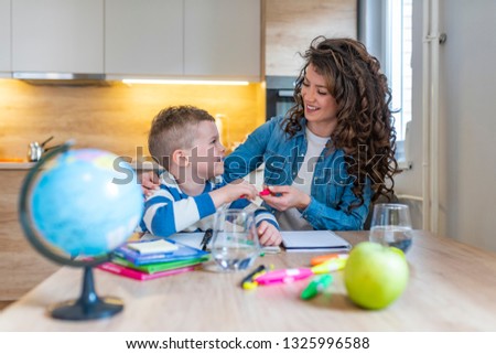 Young boy doing his school homework with his mother, at home, he is writing on a book. Mother and child son doing homework writing and reading at home