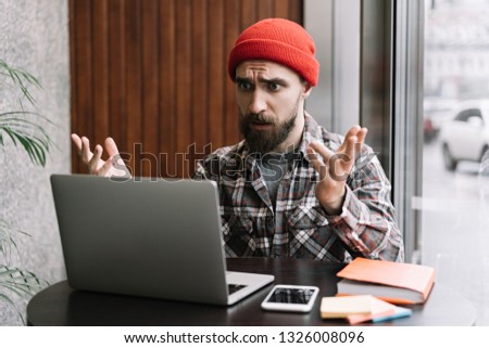 Hipster freelancer with emotional face using laptop computer, working a project in modern office . Bearded man confused and surprised while searching online information.
