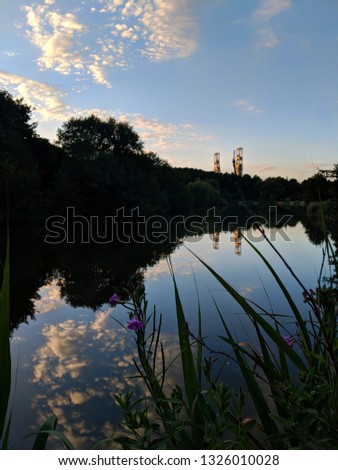 Beautiful reflections on a very still lake at twilight at Vicar Water Country Park, reeds in foreground and Clipstone Colliery Headstocks silhouetted on the horizon at Clipstone, Nottinghamshire, UK