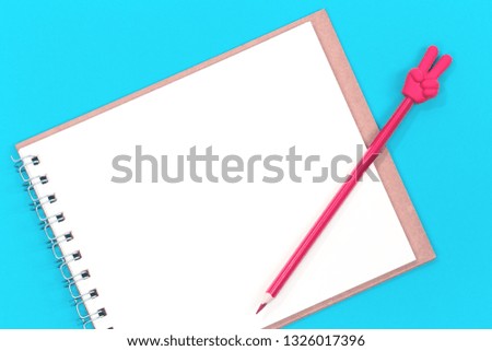 A red pencil with V sign and a blank notepad on blue background. Flat lay with copy space