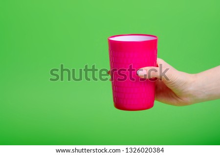 Pink plastic cup in hand on green background