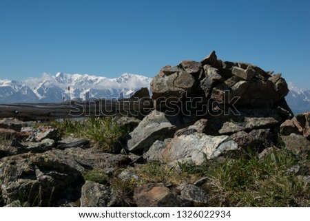 Wood and stones on the background of rocky mountain peaks covered with snow. Mountain glacier in the Republic of Altai Russia. The glacier at an altitude of 3500 meters above sea level. In focus.