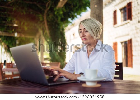 Confident senior woman typing text on a laptop computer in a cafe 