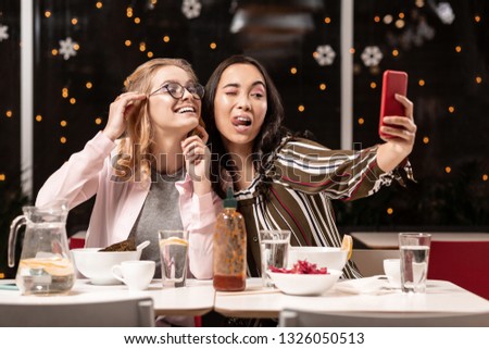 Hello from friends. Female elegant students fooling around in food spot and taking video on phone to send it to their friend lately