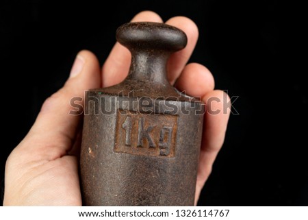 Old rusty metal weight for weighing products in the palm of your hand. Accessories for weight determination. Dark background.