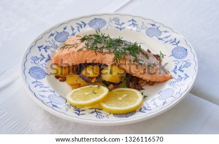 Close up picture on salmon fillet served with roasted potatoes and onion, slices of fresh lemon and chopped fresh dill on the rustic plate. Fresh, healthy, light, diet fish dish for lunch or dinner. 