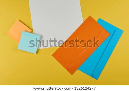  layout of office supplies: envelopes, stickers, paper clips, buttons, pen, paper on a yellow background                 