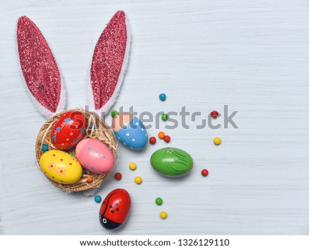 Colorful easter eggs and easter bunny ear rabbit in basket nest with colored sweets candy decoration on white wooden background top view 