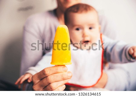 Orange ice cream in the foreground with baby in the background wishing to catch it.