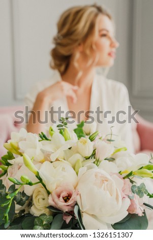 young beautiful wedding bride is sitting on a pink bed in a bright room and smiling