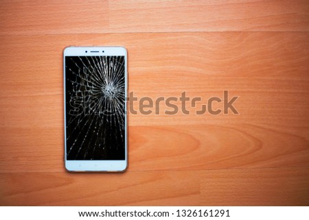 Broken phone on a wooden background. White smartphone with a broken screen