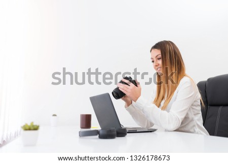 Young woman photographer sitting with computer and photography equipment and choosing best photos in modern office.