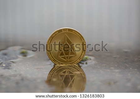 Eos cryptocurrency physical coin placed in the water on the street. Macro shot.